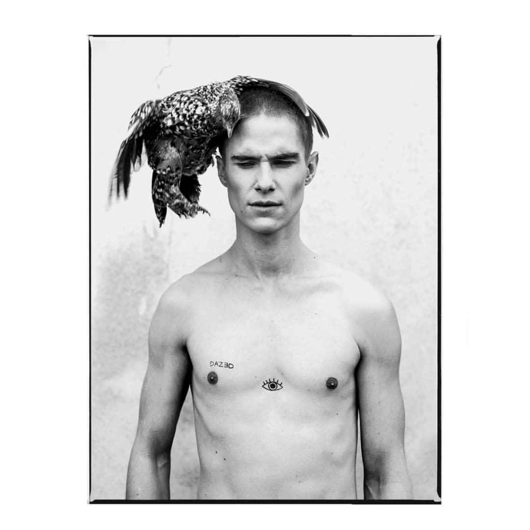 Portrait argentique en noir et blanc d’un homme torse nu portant une poule sur la tête